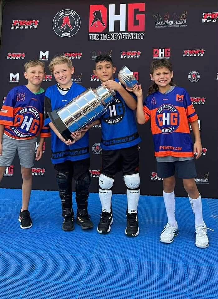 Quatre jeunes joueurs de dek hockey posent avec un trophée