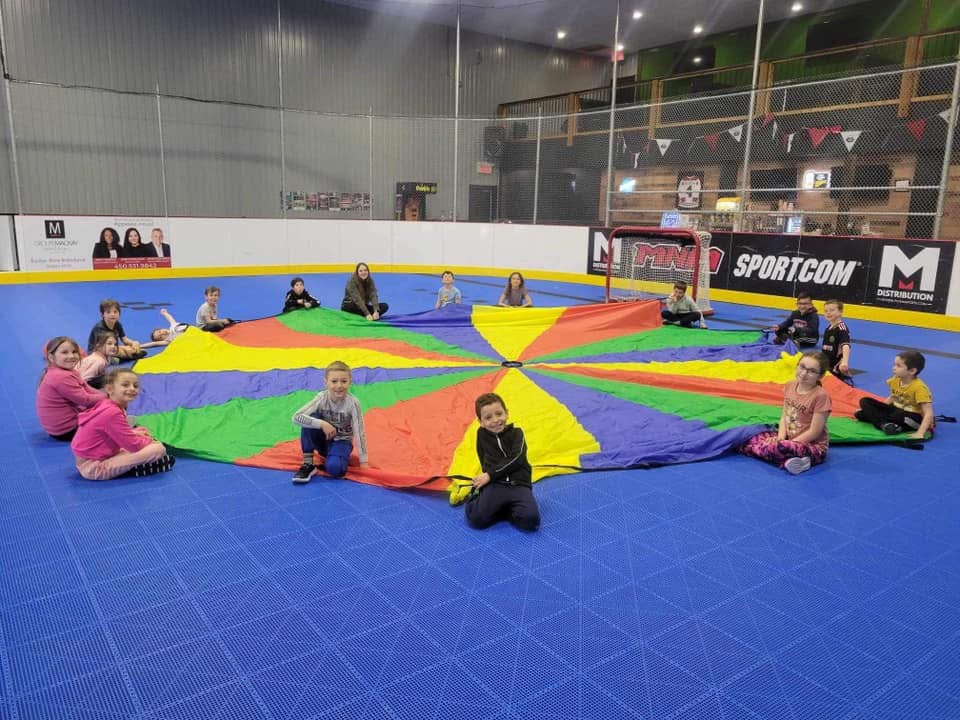 Des campeurs et une animatrice réunis autour d’un parachute multicolore au DHG