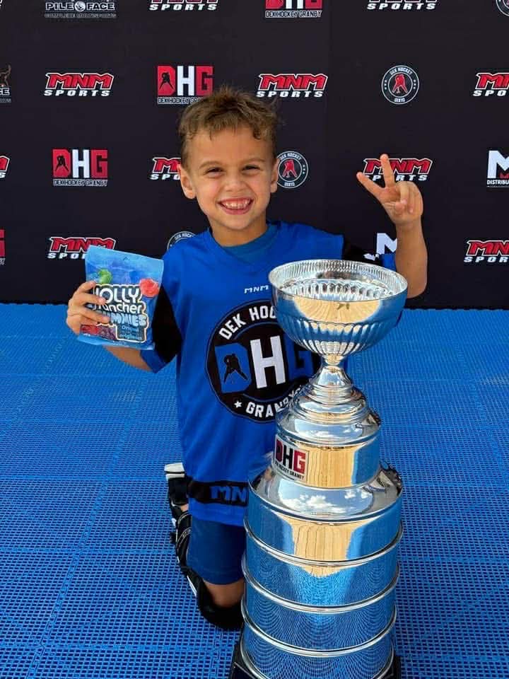 Un jeune joueur du camp DHG sourit à côté d’un trophée